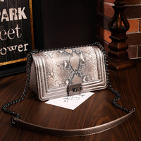 Bertha Shoulder Bag in python texture vegan leather shoulder bag with chain detail on wooden surface.